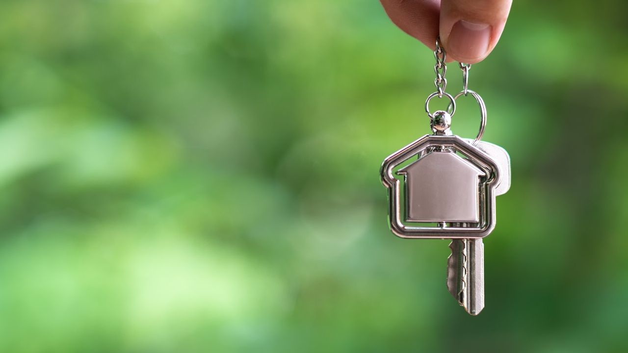 Home key with house keyring hanging with white wall background, copy space